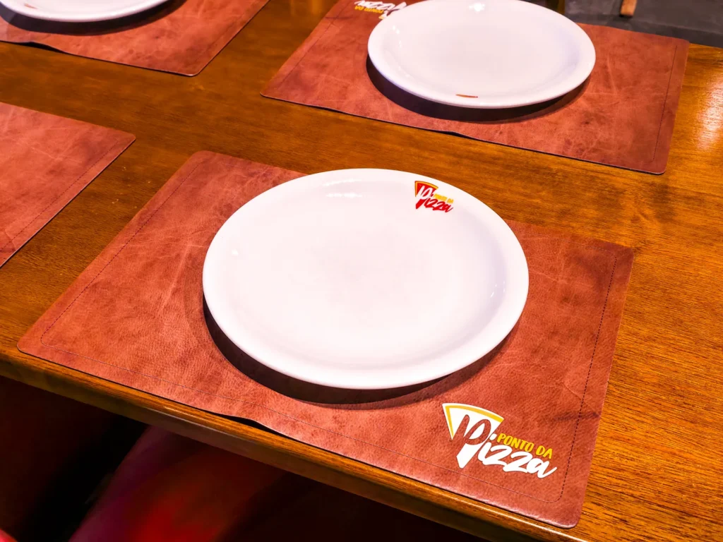 Mesa posta com prato branco sobre jogo americano com o logotipo do Ponto da Pizza